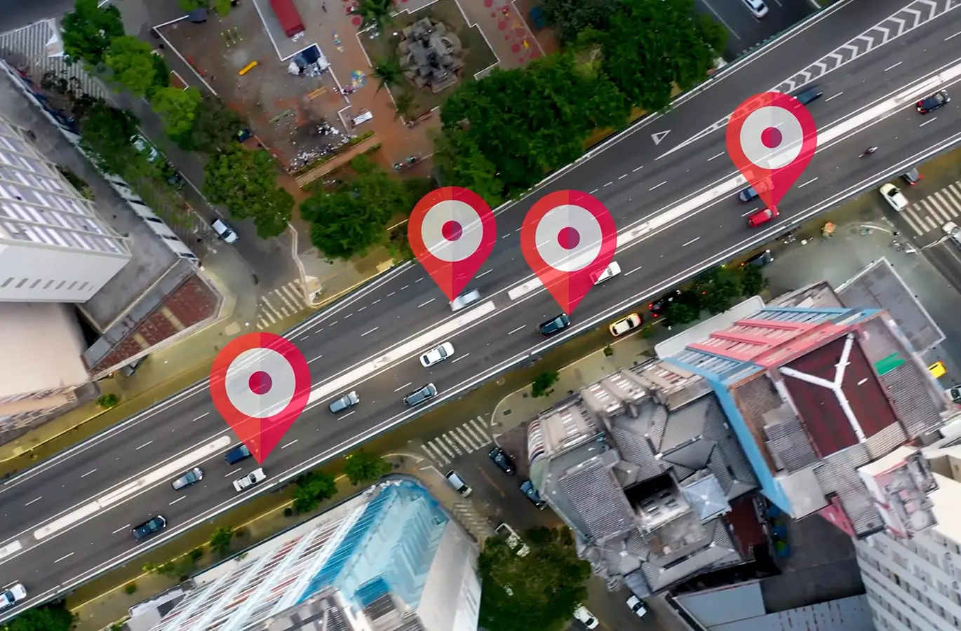 Aerial view of a busy urban road featuring multiple location markers, with vehicles and buildings surrounding the area.