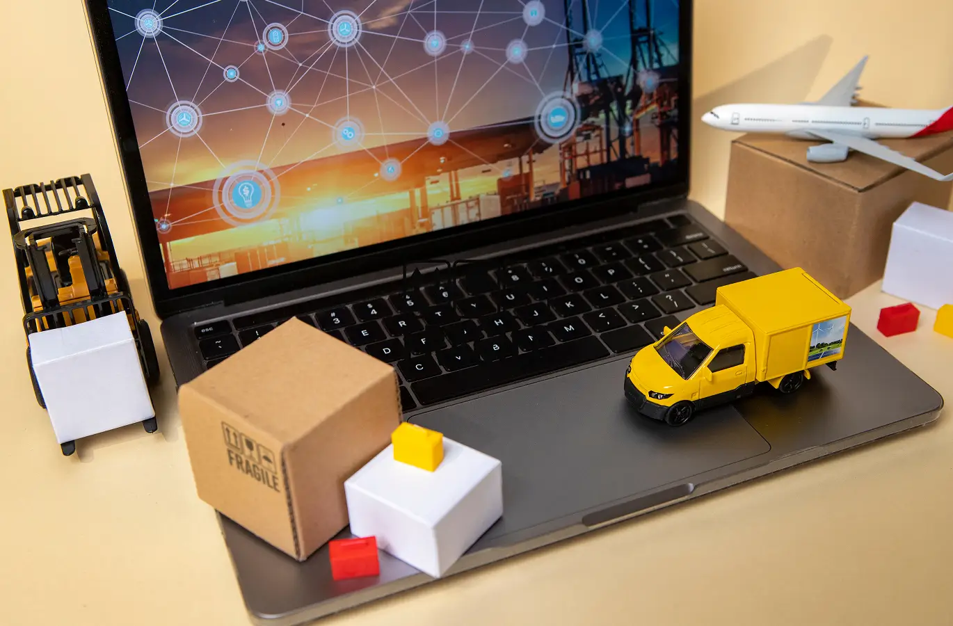 A laptop displaying a logistics interface, surrounded by mini trucks, boxes, and a plane model, symbolizing supply chain operations.